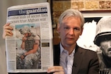 Assange, seen here looking much younger, holds up the newspaper which reads massive leak of secret fules exposes true Afghan war