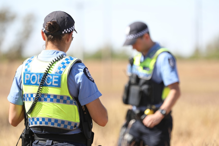 Two police stand on a road with red dirt in the background.