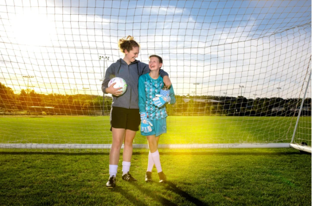 Two female soccer players standing inside the goal net with one wearing her women's specific goalie gloves 