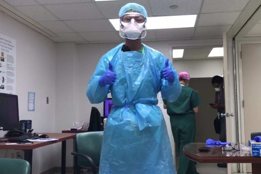 Kevin Cho Tipton, wearing mask, visor, protective overalls and gloves, gives the thumbs up