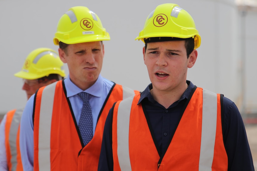 Hudson, a young man, wears PPE and a hard hat. Mr Hastie watches from behind.
