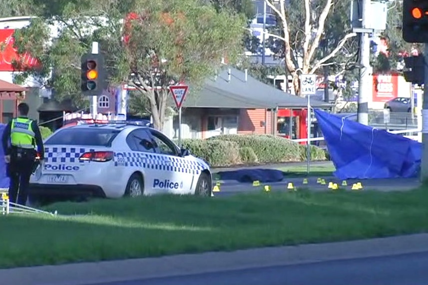 Blue tarps hang from signs on a road, as a police officer stands near a parked police car.