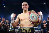 Boxer Tim Tszyu smiles at the camera, with fists clenched and a world title belt slun over his shoulder.