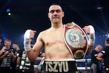 Boxer Tim Tszyu smiles at the camera, with fists clenched and a world title belt slun over his shoulder.