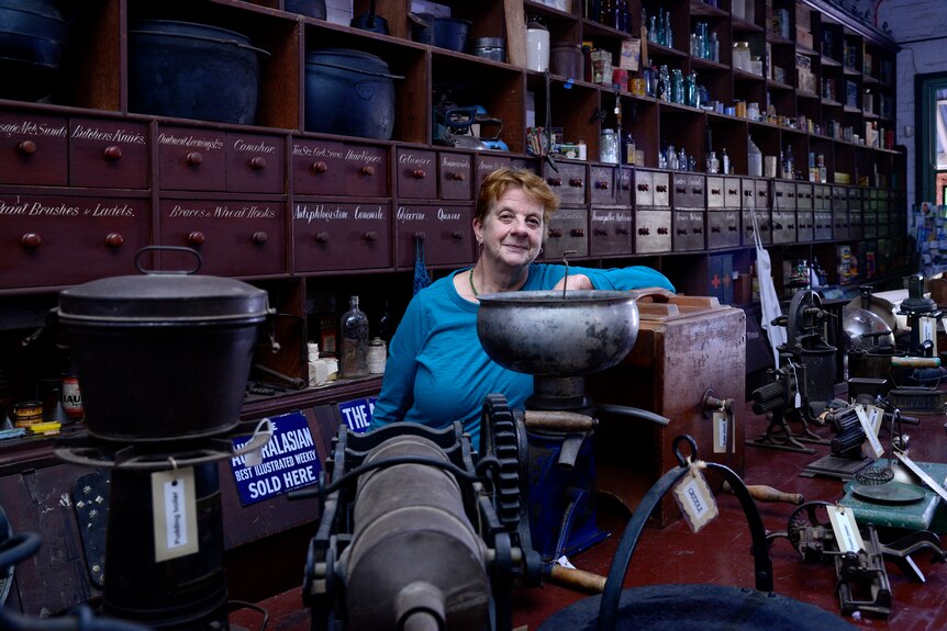 A woman in a blue long-sleeve top poses for a photo among old machinery in a pioneer museum