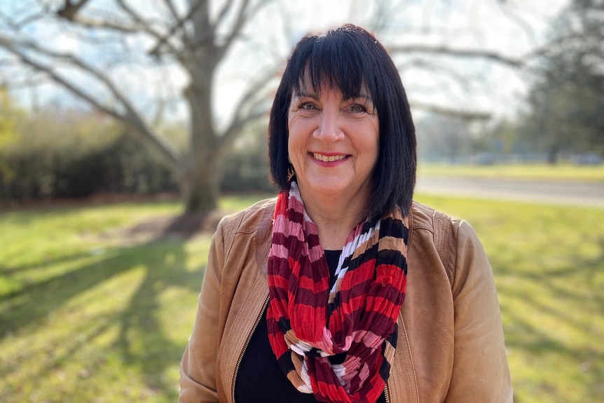 A woman stands in a park smiling at the camera.