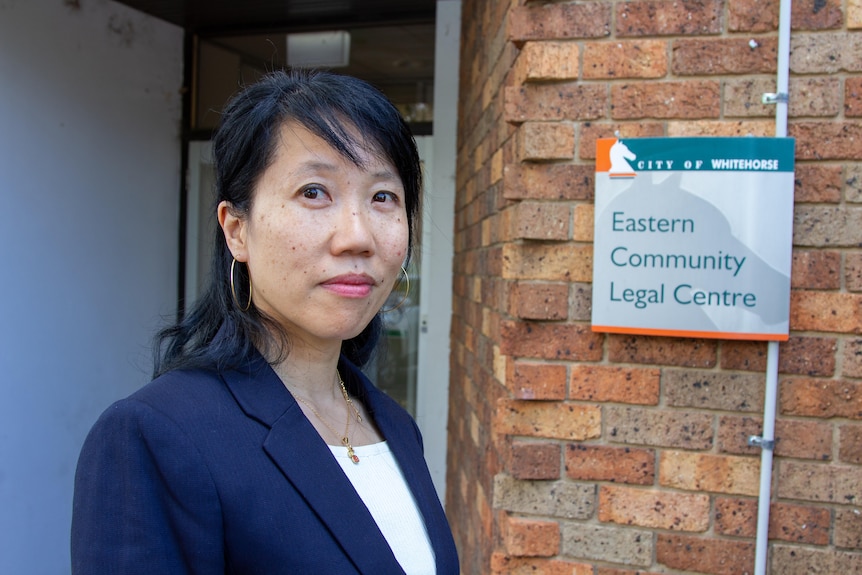 A woman with black hair and a blue jacket looks at the camera in front of a legal service sign