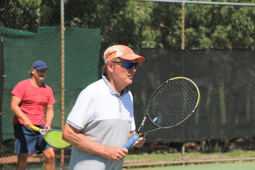 Geoff Rowbotham wearing a cap, sunglasses and t-shirt holding a tennis racquet.