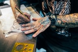 A tattoo artist with tattoos on his own hands draws a design on paper.
