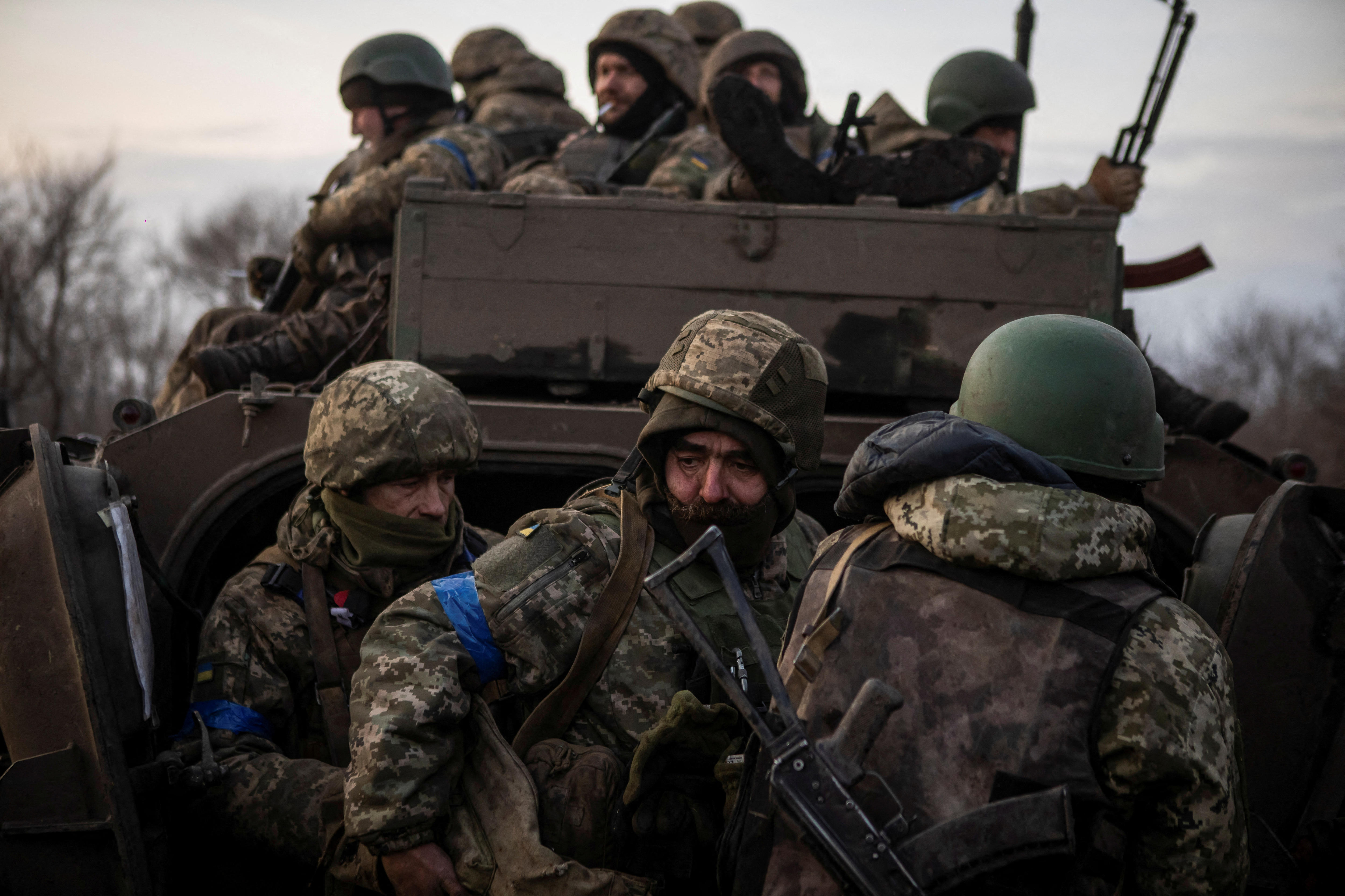 Armed servicemen gather around an infantry fighting vehicle on a road.