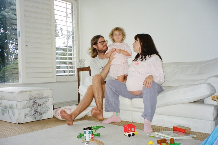 Tom, left, sits on the couch next to their son, centre, with Emily (heavily pregnant) on the right.