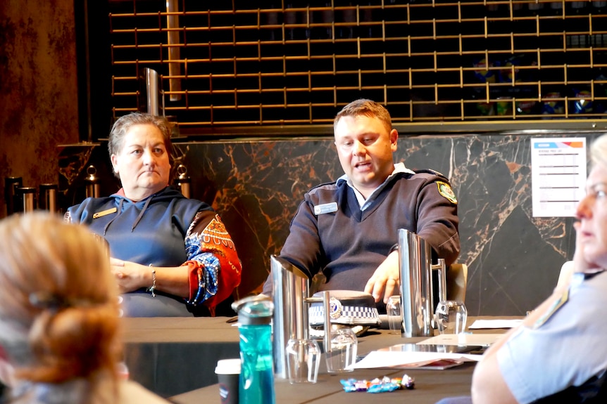 A police officer sitting in a function room, speaking to others around a table.