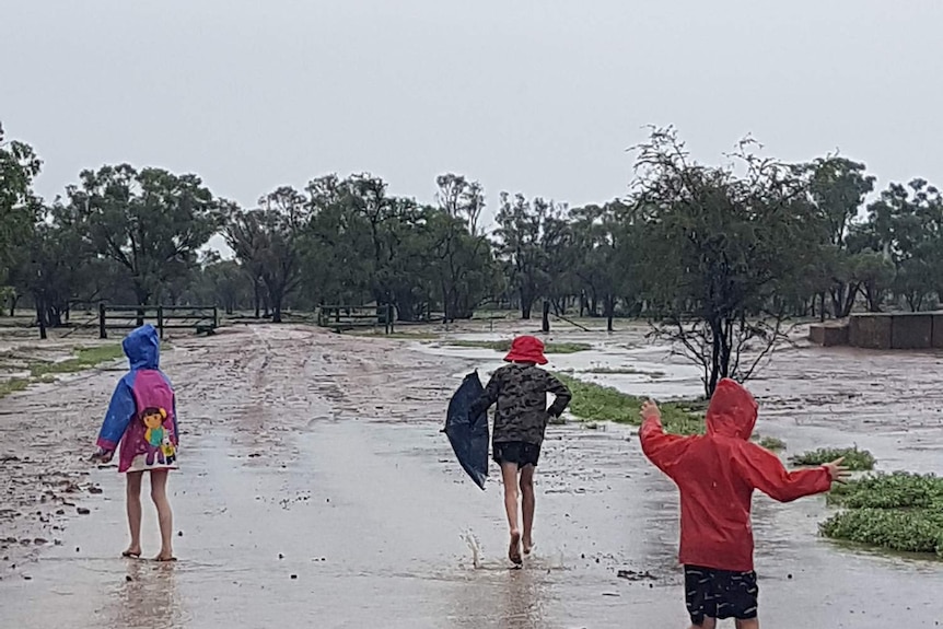 The Hawkins kids running in water in a muddy paddock, wearing colourful rain coats