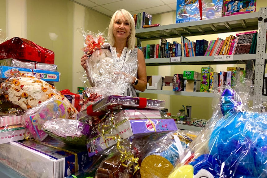 Woman standing at table and shelves full of wrapped Christmas presents