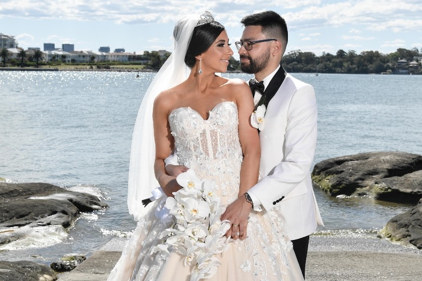 A bride and groom look at each other while standing on a boat ramp overlooking a bay.