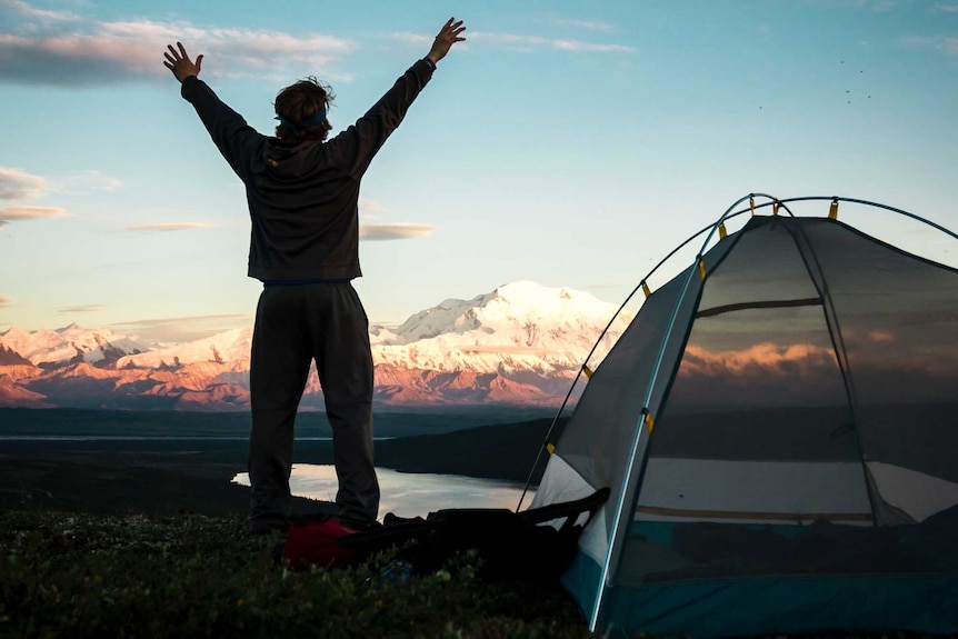 Silhouetted man standing next to a tent in the early morning