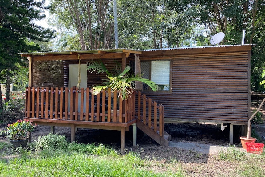 Brown timber clad cabin raised off the ground with a balcony and steps.