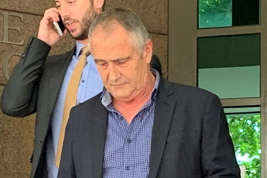 A man with grey hair wearing a suit walks down steps outside court with his hands in his pockets with others surrounding him.