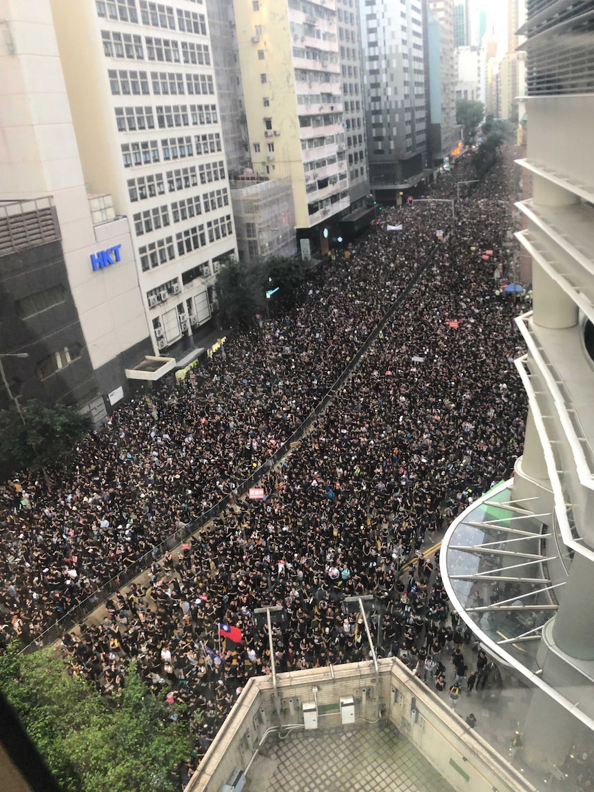 Aerial shot of huge sea of people packed onto the street snaking through high-rise buildings.
