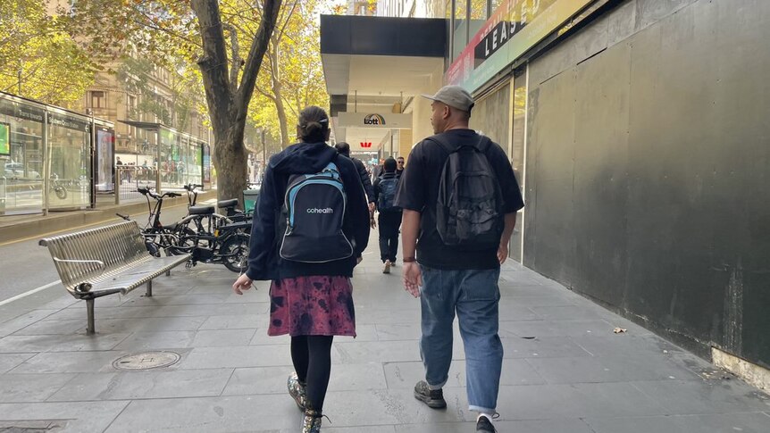 Two people walk down a CBD street, photographed from behind.