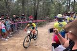 A female mountain bike rider in Australian colours heads uphill past cheering fans.