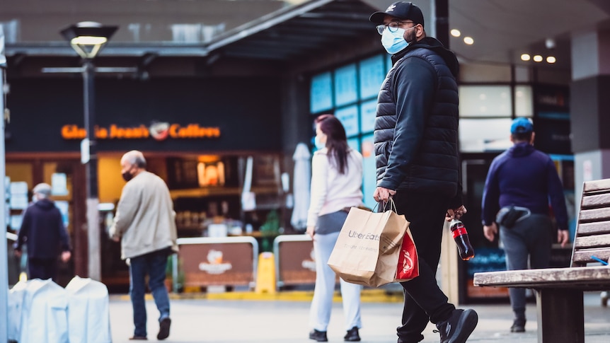 people walking along the street wearing masks and holding shopping bags