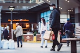 people walking along the street wearing masks and holding shopping bags