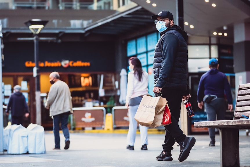 people walking along the street wearing masks and holding shopping bags