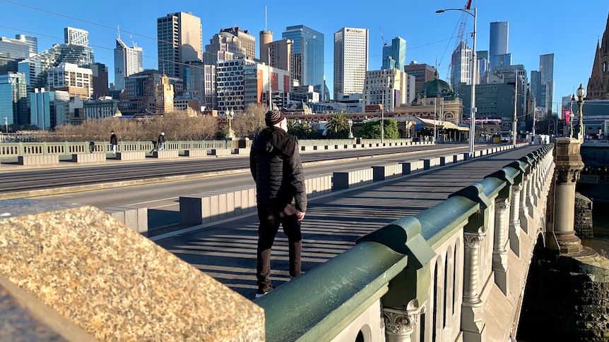 A man in a beanie walks across an otherwise empty Princes Bridge in winter sunlight.