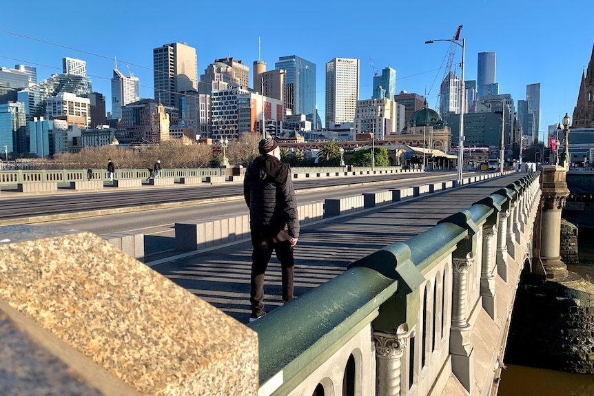 A man in a beanie walks across an otherwise empty Princes Bridge in winter sunlight.