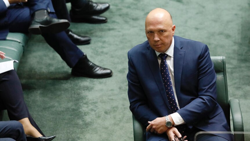 Dutton looks at the camera with a neutral expression from the house floor.