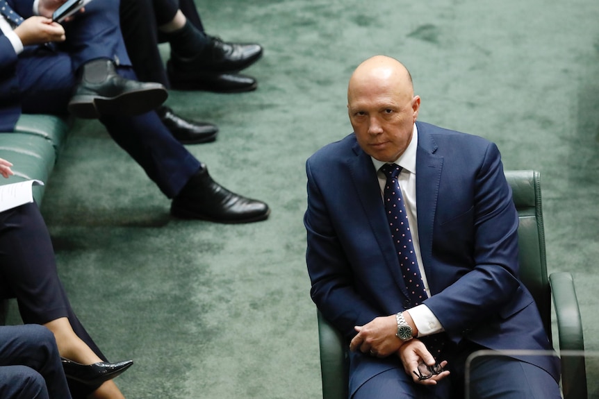 Dutton looks at the camera with a neutral expression from the house floor.