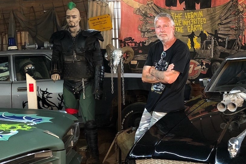 Man in black t-shirt in front of Mad Max memorabilia.