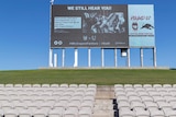 Empty seats and a scoreboard are seen near the grass banks of Jubilee Stadium