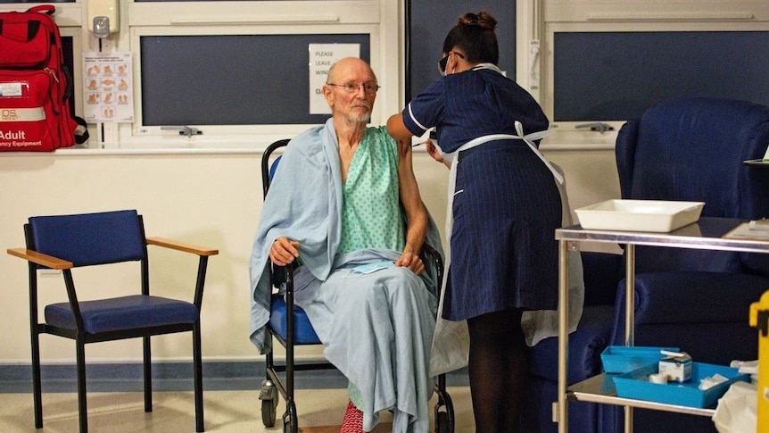 A nurse leans over an elderly man, giving him an injection in his left arm. 
