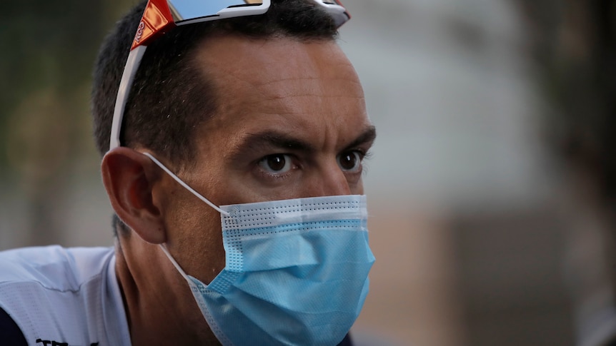 Richie Porte wears sunglasses on top of his head and wears a blue medical mask