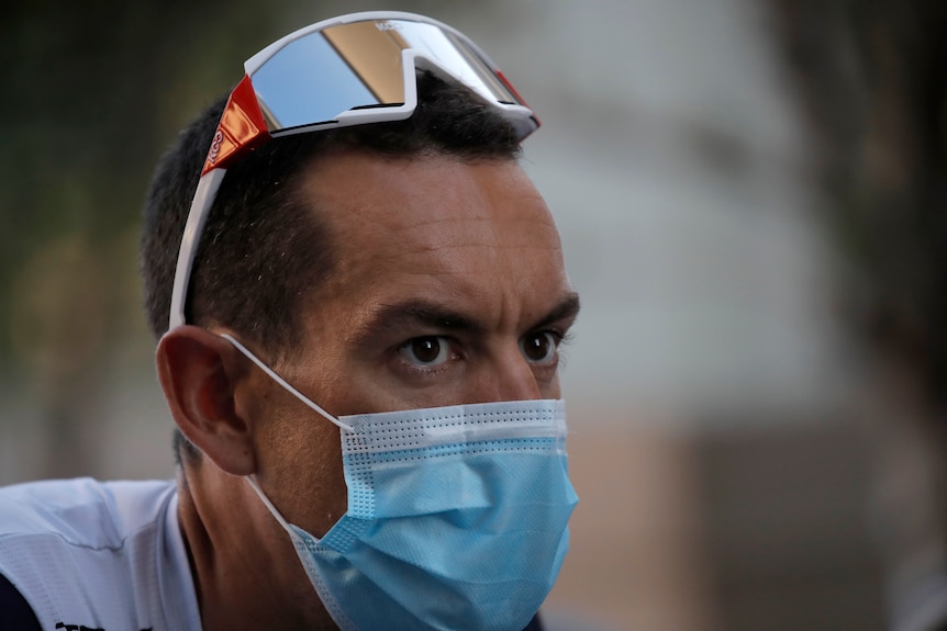 Richie Porte wears sunglasses on top of his head and wears a blue medical mask