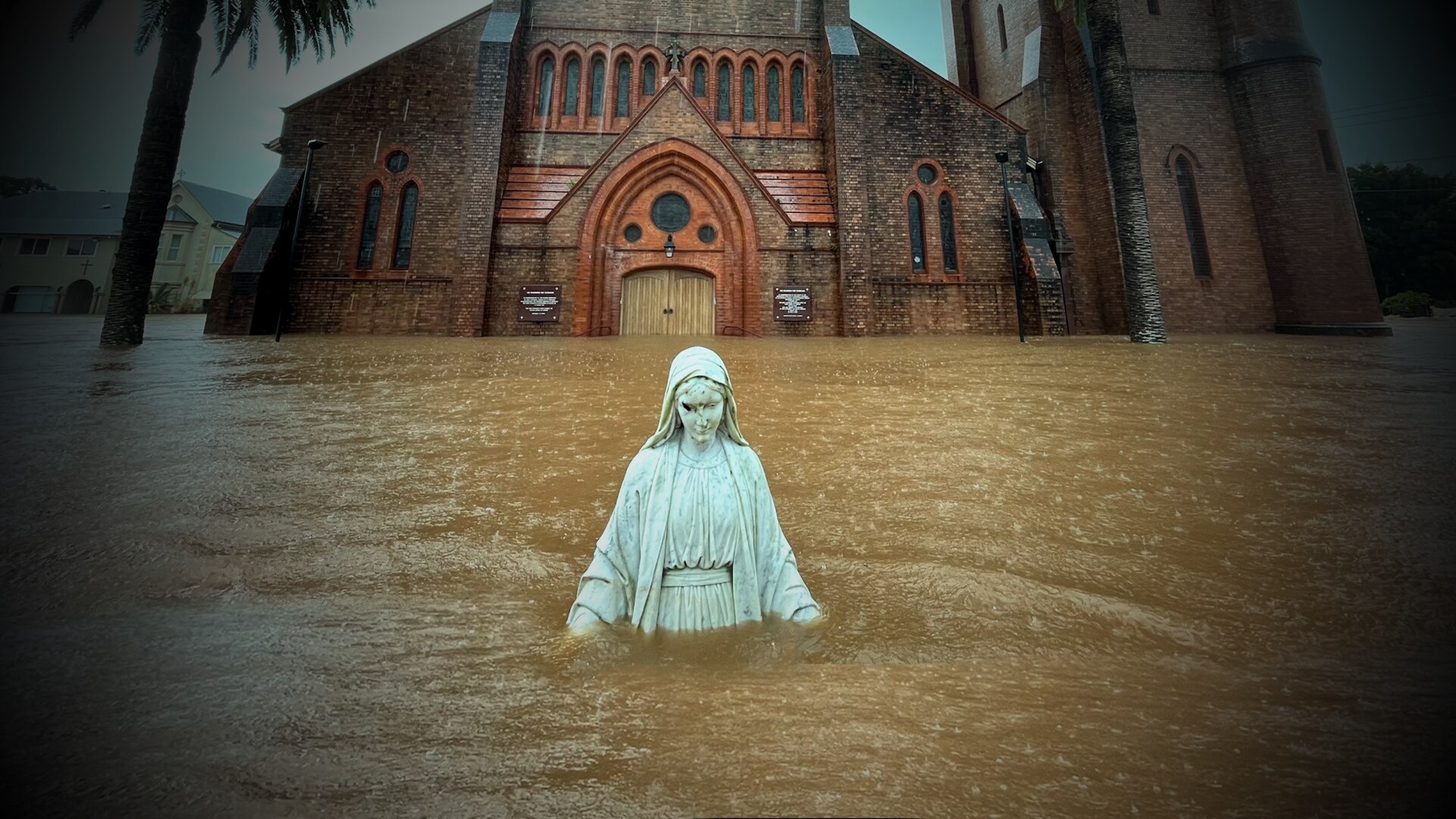 A statue is isolated in front of a church surrounded by floodwater.