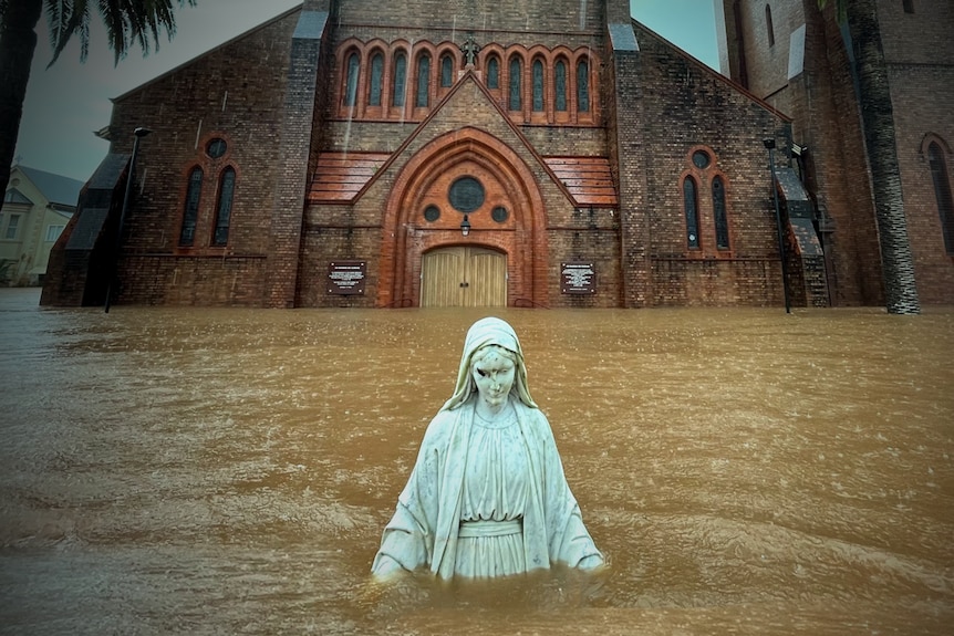 A statue is isolated in front of a church surrounded by floodwater.