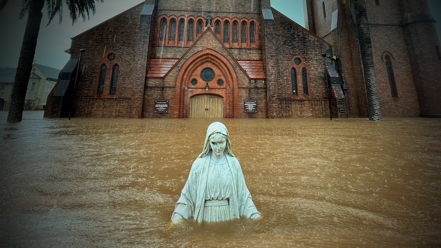 A statue is isolated in front of a church surrounded by floodwater.