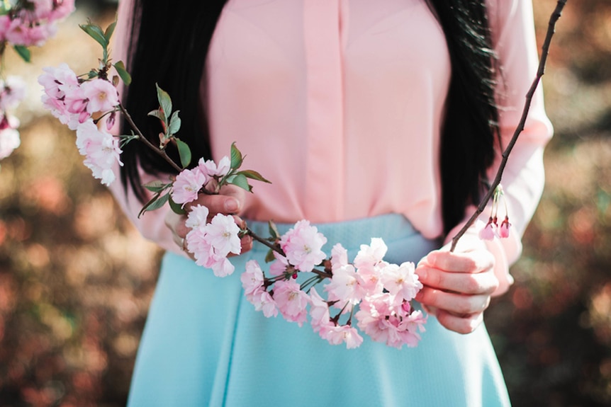 A woman holds a stem of flower blossoms.