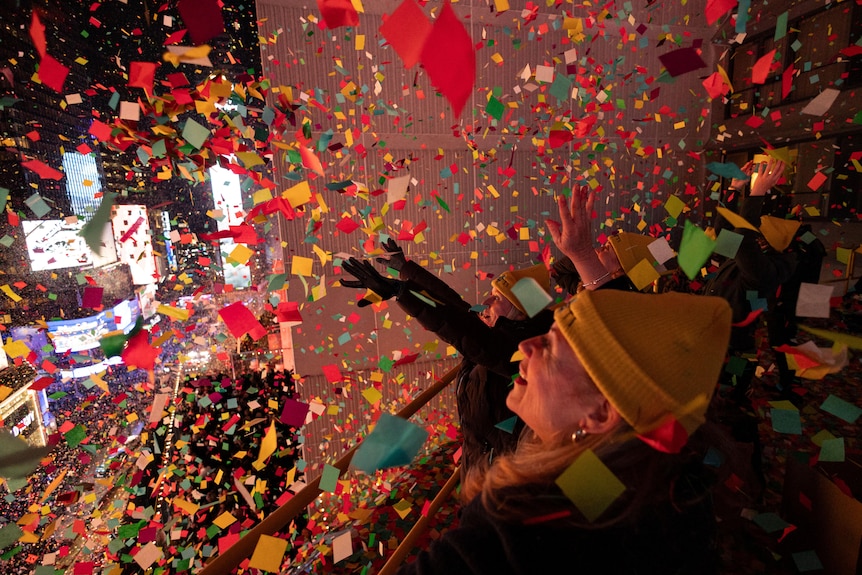 A woman smiles as she drops colourful pieces of confetti from a building.