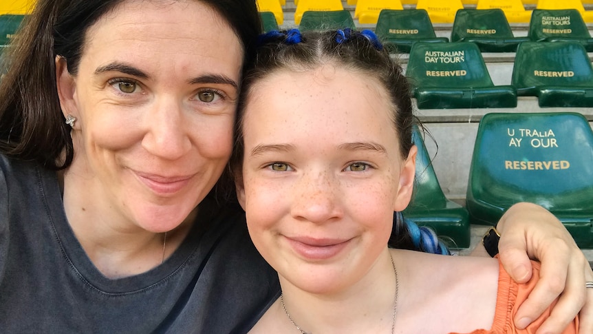 A mother with dark long hair is sitting closely with her a young girl with freckles