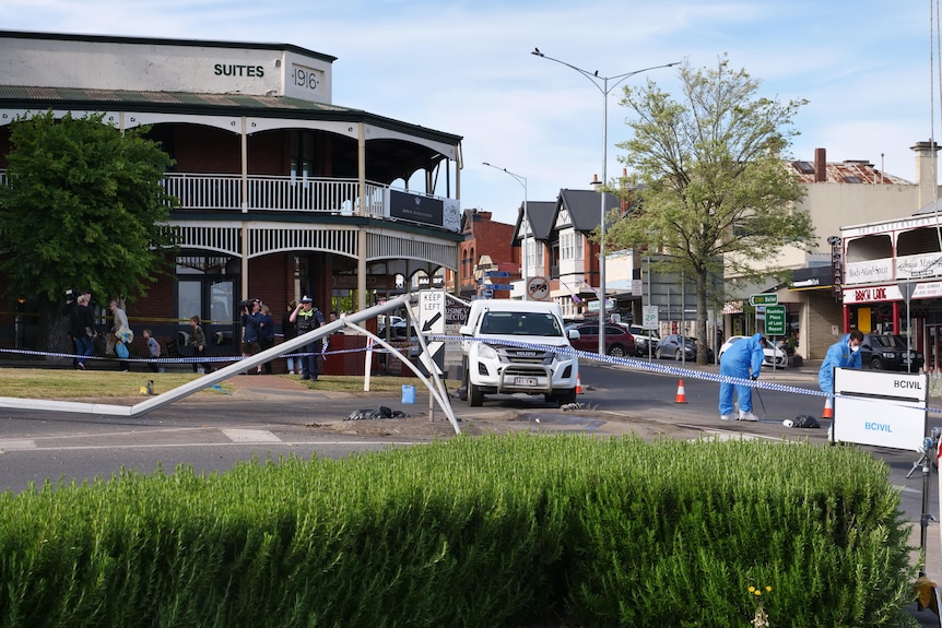 A hotel with police tap blocking off the area and road, while investigators wearing blue hazmat suits comb through debris