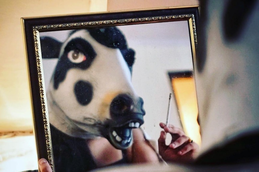 A woman looks into a mirror wearing a cow mask.