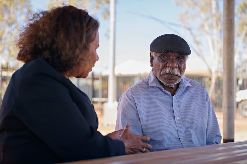 Leanne Liddle and Warlpiri Elder Ned Hargraves sit down at a table in a Yuendumu park.