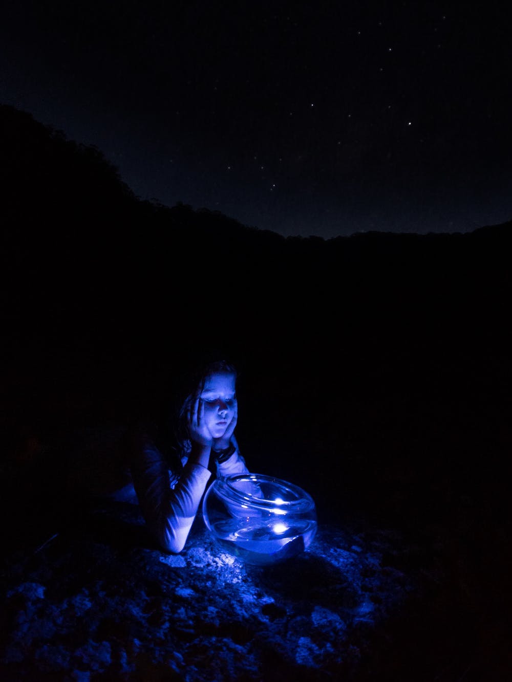 A young girl looks into a glass bowl on a mossy rock