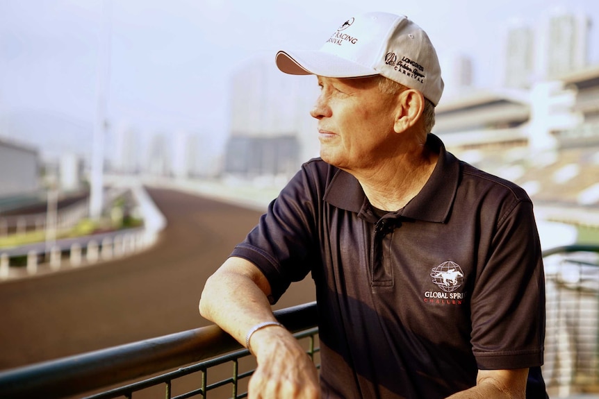 John Moore wearing a black polo shirt and white cap leaning on a green rail.