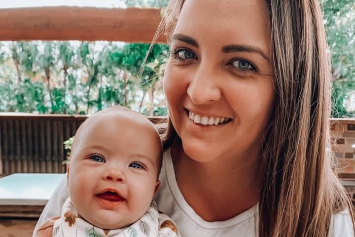 Brunette woman and her baby both smile at camera