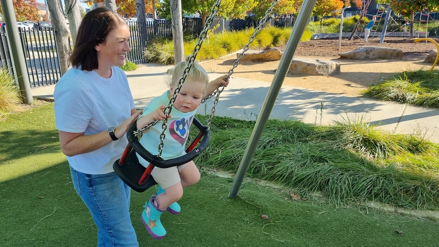 A woman with a brown bob pushing a young girl with blonde hair on a swing.